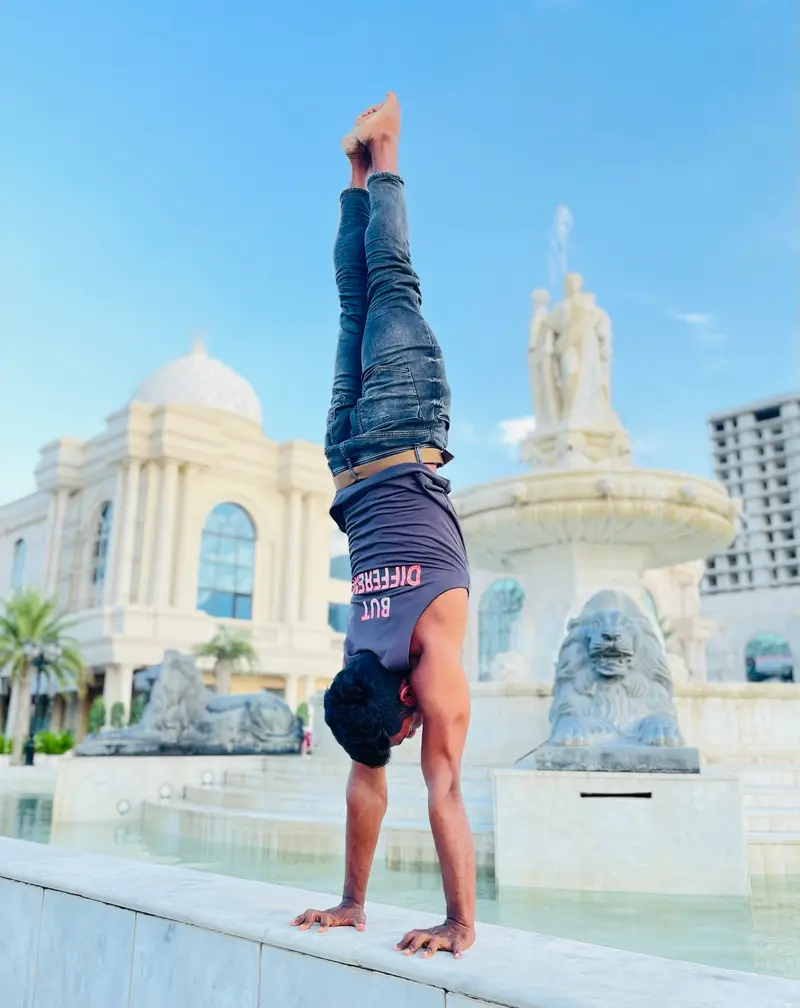 Manoj holding a freestanding handstand beside a fountain